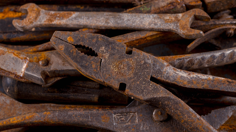 A rusty old set of pliers sits on top of a pile of old tools