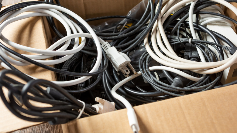 Mismatched extension cords and cables are piled in a cardboard box