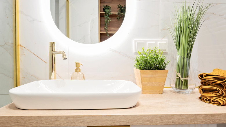 A stylish bathroom basin with plants, liquid soap, and towels