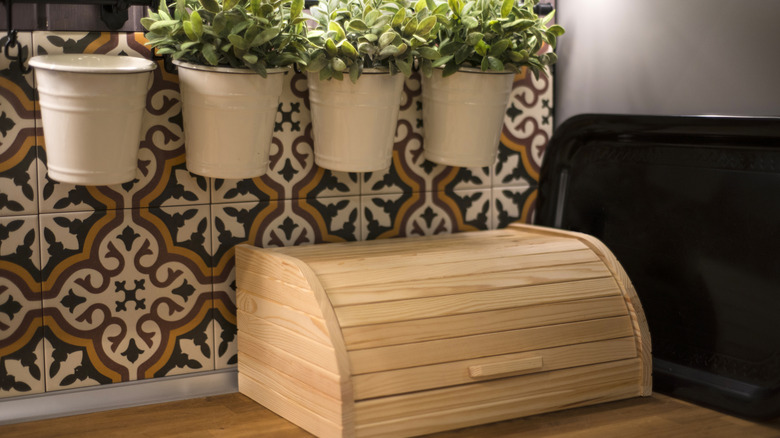 Wooden bread box in kitchen with colorful tiles and herb planters
