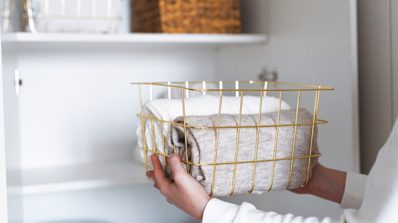 Woman putting a bin containing folded towels on an open shelf