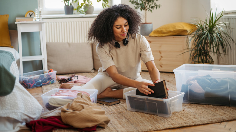 A smiling woman putting items in plastic boxes while decluttering her home