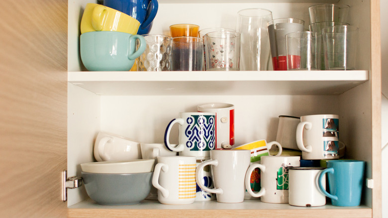 Stacked coffee mugs in disorganized cupboard