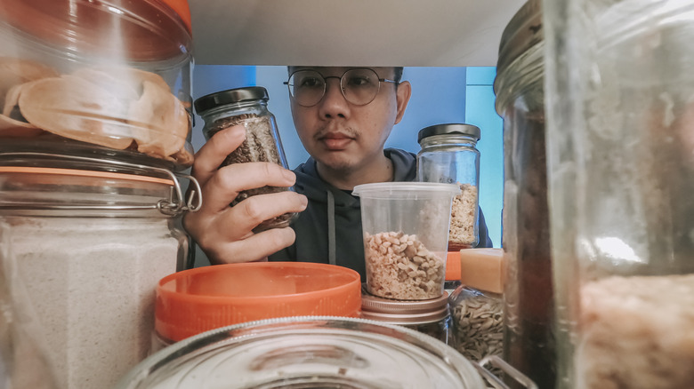 Inside cabinet view of man pulling jars out of cluttered cabinet