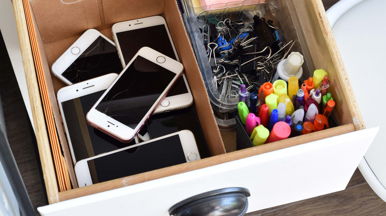 Open drawer full of old phones and office supplies.
