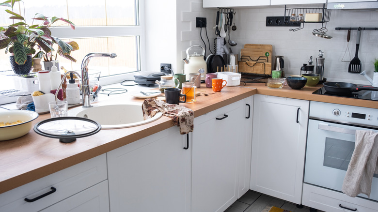 A modern but dirty kitchen with counters covered with plates, mugs and other drinkware