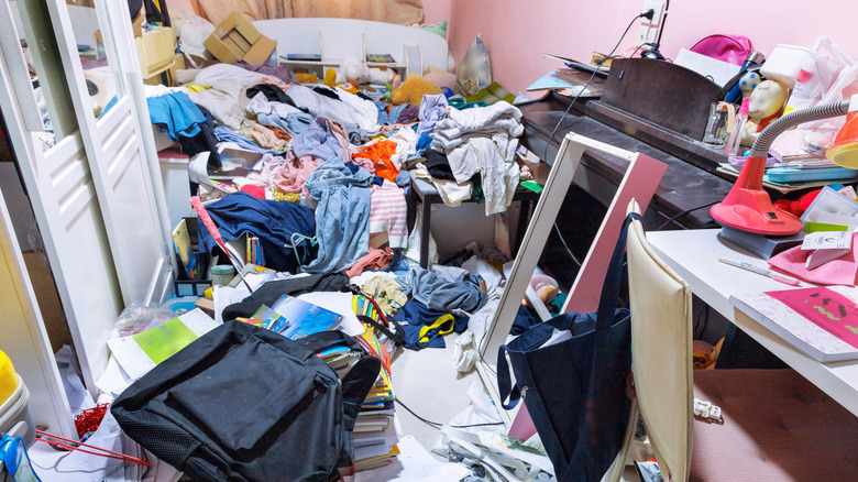 Very messy bedroom with clutter including clothing and boxes