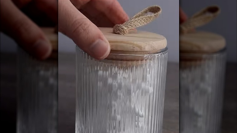A hand putting the lid from a candle onto a glass filled with cotton swabs