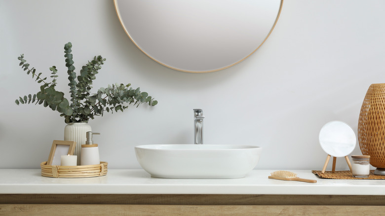 A well-organized bathroom countertop with baskets, mats, a brush, lotions, and candles