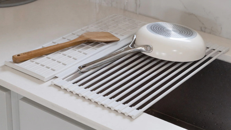 A clean white saucepan dries on a rollable dish rack.