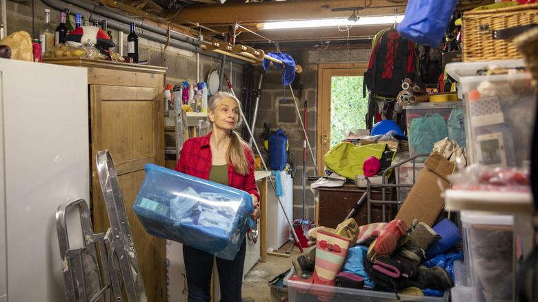 Woman carrying box into an unorganized garage, looking for a place to store it.