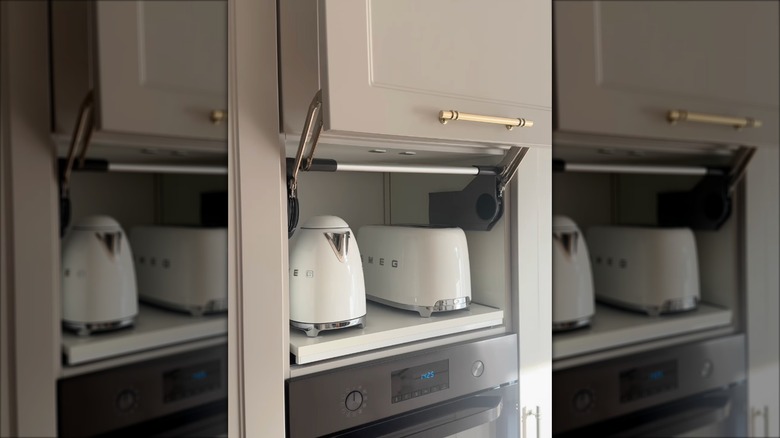 A shelf for appliances inside of a cabinet holding a white SMEG toaster and kettle
