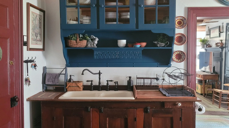 A blue wall-hung hutch holds dishes and décor above a kitchen countertop.