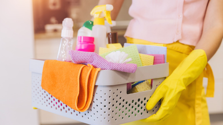 Hands in yellow rubber gloves hold a caddy of cleaning supplies