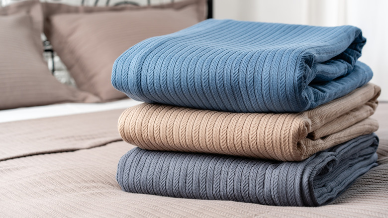 A stack of three different blankets on a bed