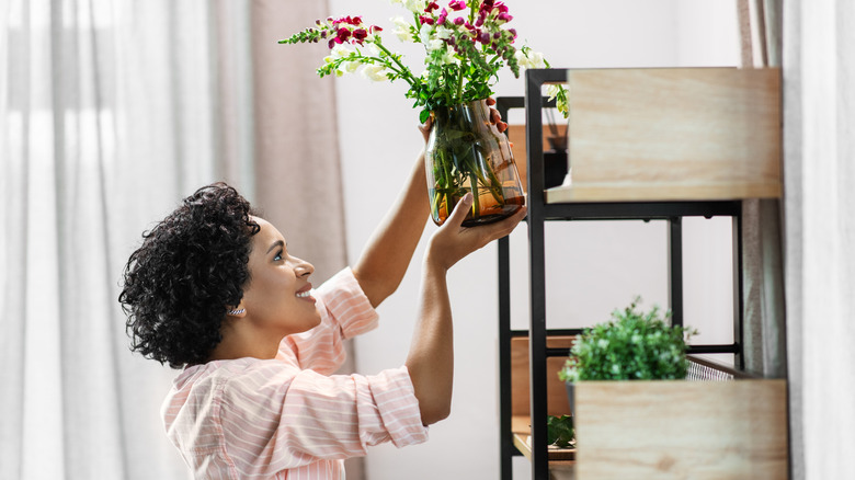 Woman putting a vase with flowers in it on her shelf