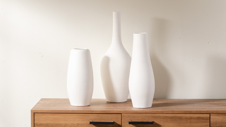A timber cabinet with three white ceramic vases on display