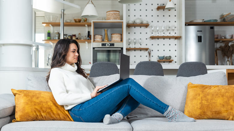 woman on couch working on laptop with kitchen in the background