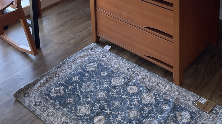 Small Persian-style rug next to a dresser, curling at edges
