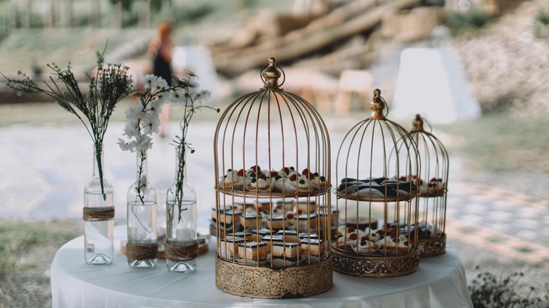 Small pastries are displayed inside gold birdcages next to three bud vases