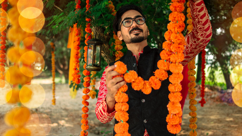 A young Indian man hangs a flower garland made from marigolds from a tree