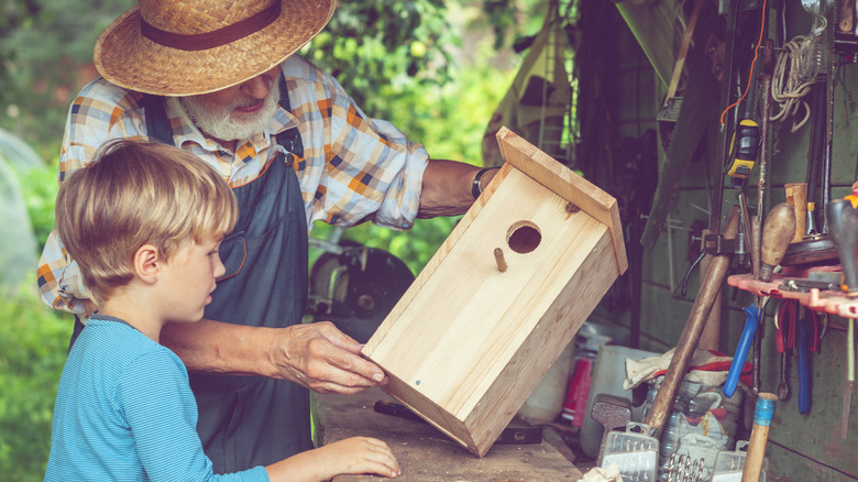 A grandfather and grandson prepare to decorate a wood birdhouse.
