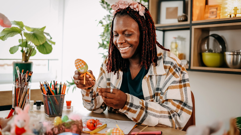 Woman smiling and holding Easter egg in front of craft supplies