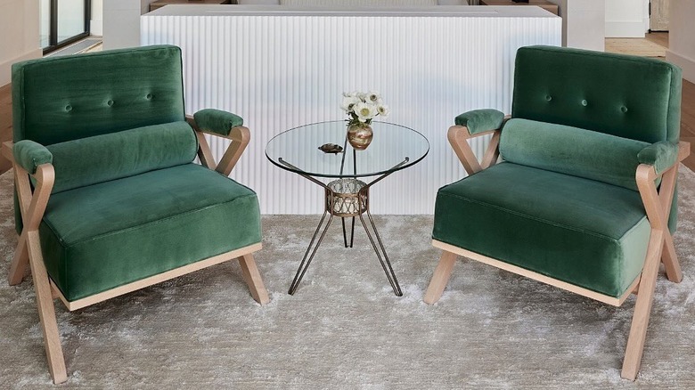 Two accent chairs upholstered in bottle green velvet and a glass side table