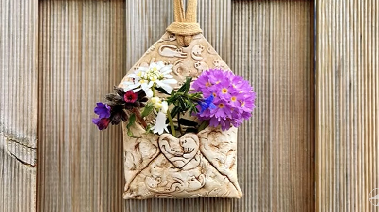Envelope made of clay with textured patterns on it and flowers tucked inside