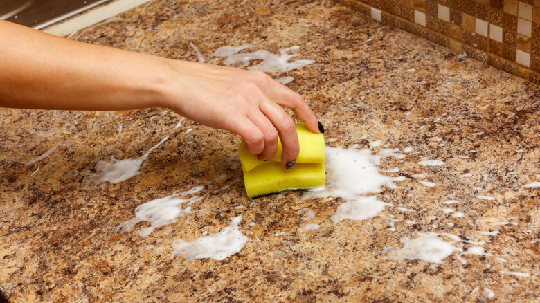 Person's hand wiping countertop with sponge