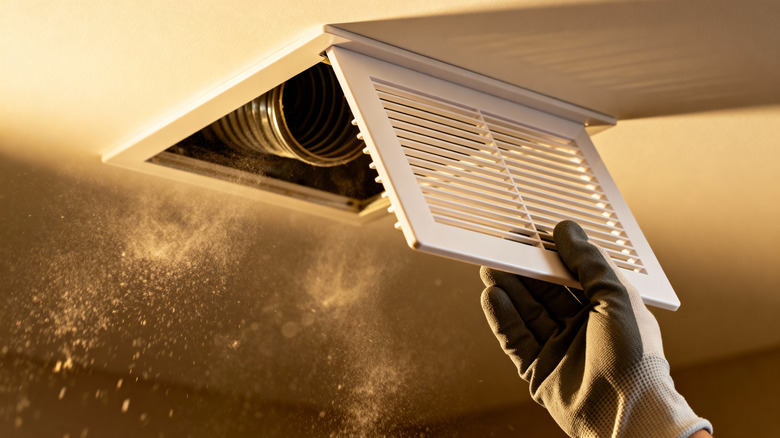 A gloved hand removing a dirty air vent cover