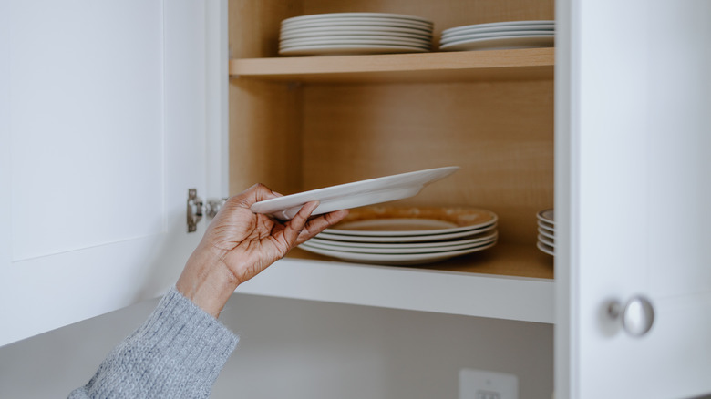 person grabbing a plate from a kitchen cabinet