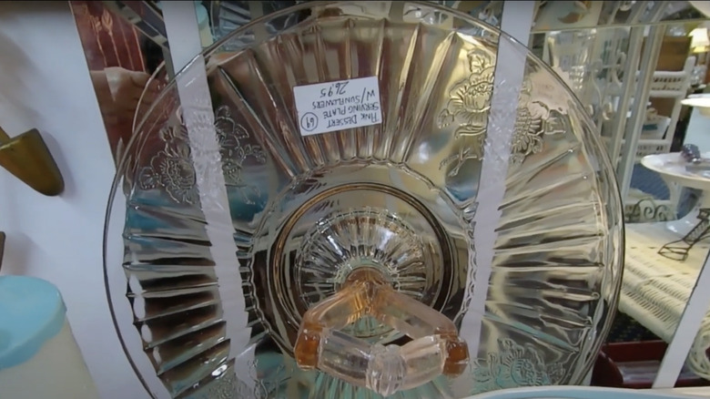 A pink serving plate in the Mayfair or Open Rose pattern by Hocking Glass Company sits on a shelf in a thrift store.
