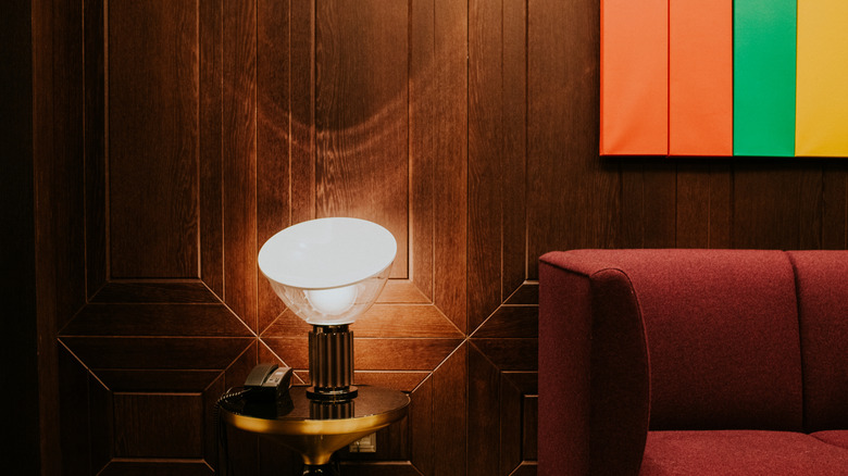 Close up of wood paneling behind a sofa and end table, a lamp, and phone