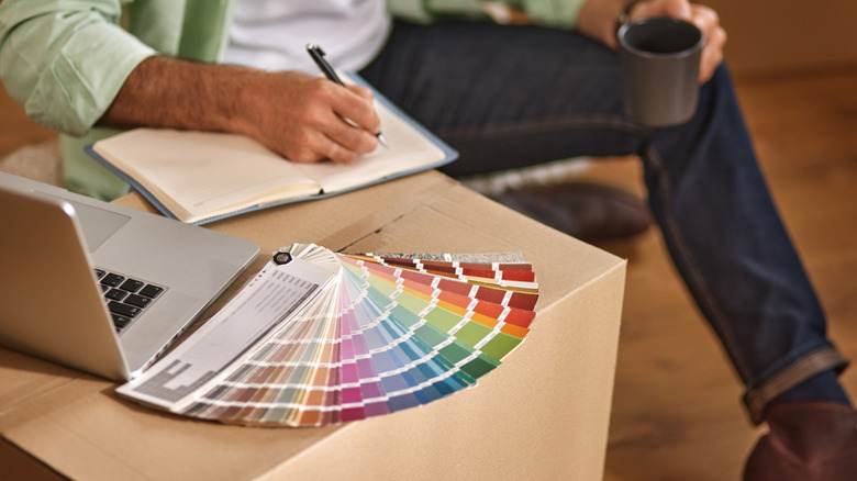 A man writes in a notebook next to an array of paint chips.