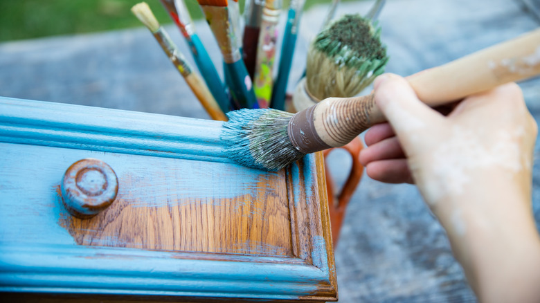 Close up of a hand painting a wooden drawer blue.