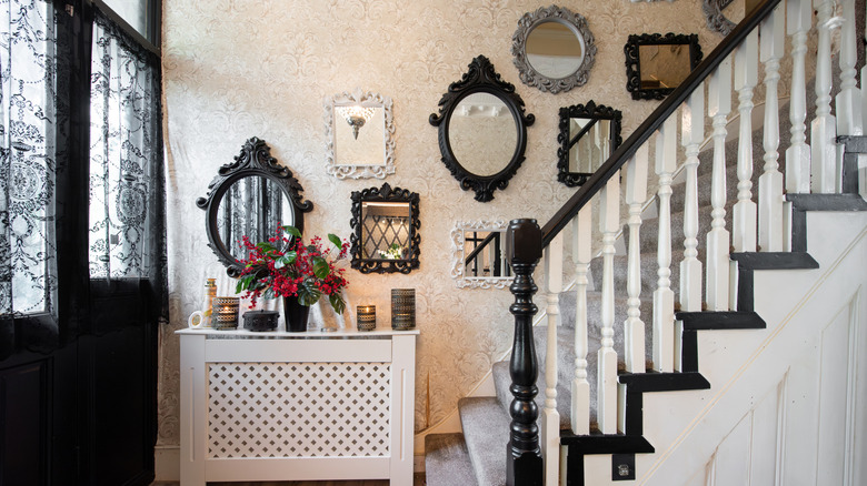 An entryway has a console table decorated with flowers and candles while mirrors hang on the wall along a staircase.