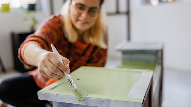 Woman painting cabinet drawers green