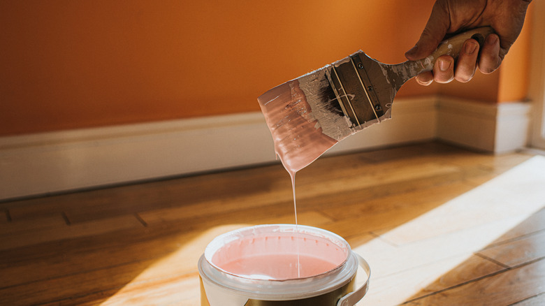 A hand holding a dripping paintbrush over an open paint can