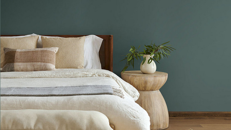 A bedroom with cream and neutral bedsheets and Hidden Gem by Behr painted on the wall