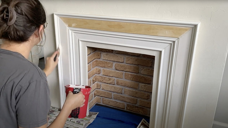 A person painting the surround of an imitation fireplace