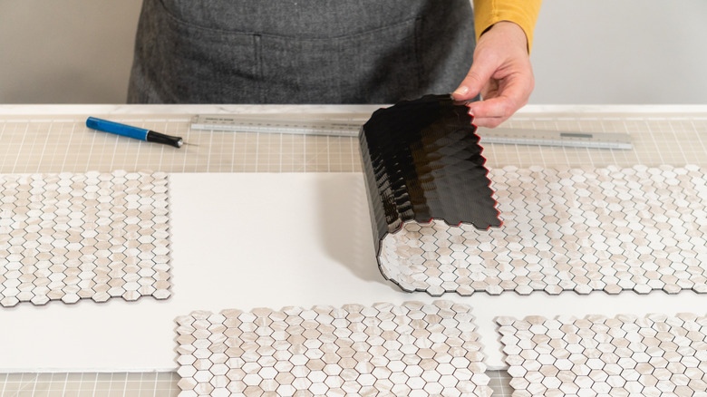 A person applying peel and stick tile to a backing surface