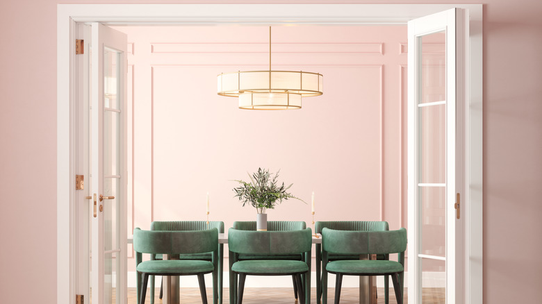 A chandelier hangs over the table in a soft pink dining room
