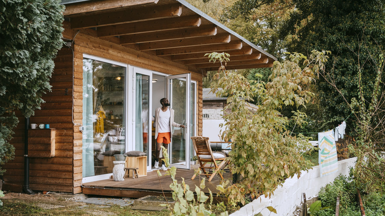 Man standing on the porch of a tiny house enjoying the view.