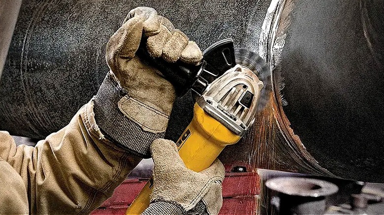Close-up of a person cutting through a large metal pipe with a DeWalt angle grinder