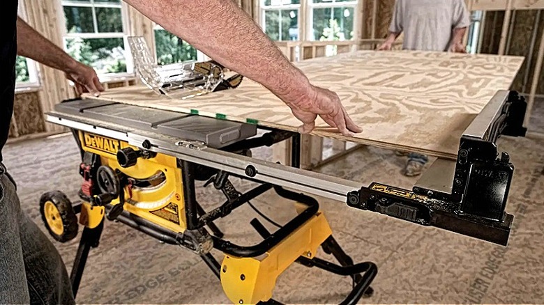 A pair of workers hold a piece of plywood in place while using a DeWalt table saw