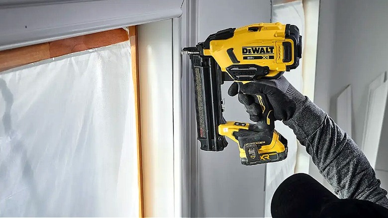 Close-up of a hand holding a DeWalt brad nailer to install window trim