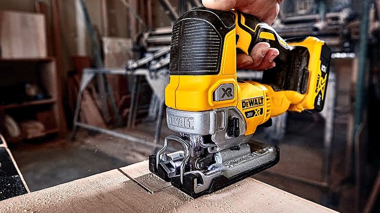 Close-up of a person using a DeWalt jig saw to cut off the corner of a lumber sheet
