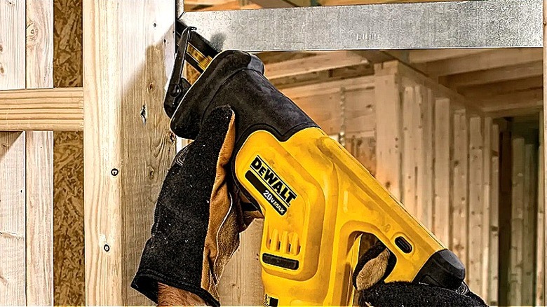 Close-up of a person using a DeWalt reciprocating saw to cut inside a tight space between metal and wood