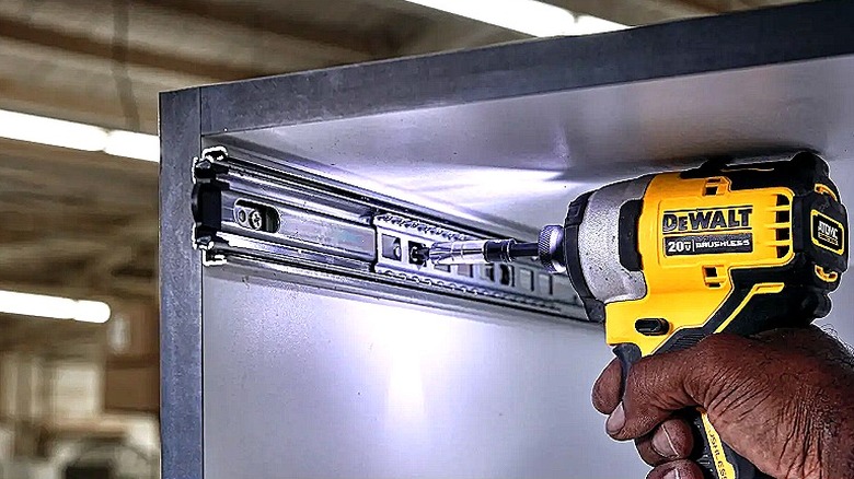 A hand using a DeWalt impact driver to install hardware inside a cramped cupboard